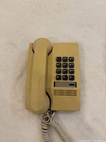 Front view of telephone with handset on base showing keypad and coiled cord