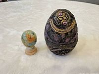 Metal egg and ceramic egg on base side-by-side