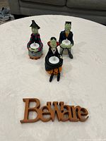 Group shot of all three figurine candle holders with LED tea lights and wood ‘Beware’ sign