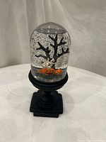 Front view of Halloween snow globe on pedestal base showing tree, jack-o-lantern and glitter