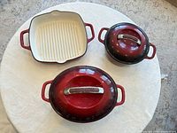Three red enameled cast iron pieces: square grill pan, oval Dutch oven with lid, round Dutch oven with lid