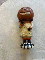 Front view of pumpkin-head figurine, showing dress, base, and facial details