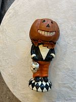 Full view of standing resin figurine showing pumpkin head, outfit, skull pail and harlequin base