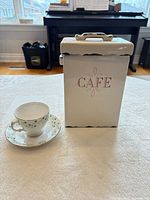 Teacup on saucer beside Café canister with lid