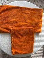 Two orange cotton bath towels laid out showing full size and folded view