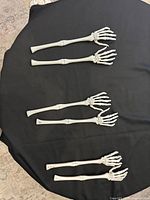 All six white plastic skeleton arm decorations laid flat on black background