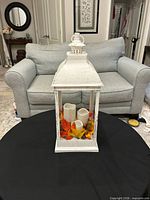 Front view of white distressed lantern on table showing candles and leaf filler