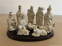 Full view of 11 white porcelain nativity figurines with gold accents arranged on dark wood base