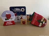 All items in lot: two Peanuts tins, two fabric hot pads, wood stamp, two plastic cups