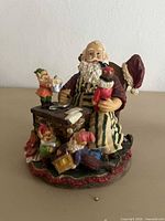 Front view of painted resin Santa workshop figurine showing Santa, elves, desk, toys