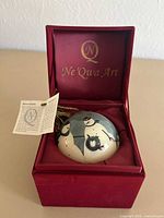 Ornament seated in open Ne'Qwa Art presentation box with tag and info card visible