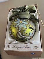 Glass ornament in Designer Series box showing glitter floral design and ribbon hanger