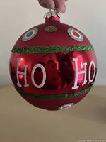 Full view of red glass ornament showing "HO HO" text, glitter bands, cap
