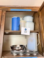 Cabinet shelf with pitchers, storage containers, fry pan and muffin pans visible