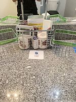 Overall view of three wire baskets on countertop containing toilet paper rolls, boxed soap and small boxed first-aid/toiletry items