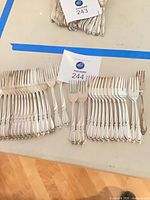 Grouping of 32 matching forks arranged by size with lot card 244 visible