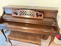 Full piano closed with brand badge visible, bench in view
