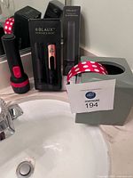 Overall lot on bathroom counter: boxed BLAUX bidet, XL tank box, flashlight, tissue box cover with headband