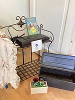 Overall lot showing bakers rack, lace skirt, VHS rewinder with FernGully tape, media storage case, shot glasses in box