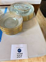 two stacks of round gold-rim pressed glass plates next to an oval gold-rim dish