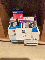 All items grouped: two HP 35A toner boxes, HP 243 ink pouch, G&G NE-T0603 M ink box, video head cleaner cassette