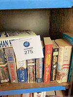 Books on shelf with lot tag, showing John Jakes and Michael Connelly titles