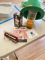 Full lot view showing hat, pill container box, tall glass, Mad Libs book, kaleidoscope case and stand