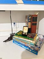 Overall lot showing tie pin in box atop stack of books with three additional books standing behind