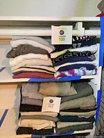 Two stacks of folded men’s tops on shelving, lot cards visible