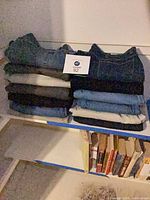 Two stacks of folded men’s pants on shelf, various colors