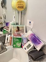 All items grouped on bathroom sink: denture cleanser, cotton rounds, blood pressure monitor, long-handled sponges, towel, manicure tools, packaged linen