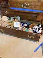 Open drawer containing mixed plush animals including koala, cow, bears, dog