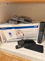 Boxed Brother ADS-1200 scanner with stacked ribbon packs, stapler, fax film roll on shelf