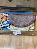 Drawer containing brown woven half-round placemat atop stacked yellow fabric, blue-white patterned fabric and other textiles