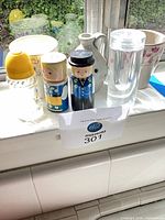 All items grouped on windowsill: wooden Dutch shakers, glass shaker with yellow lid, clear glass bud vase, grey fish bud vase, white floral planter