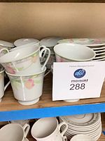 Stacked flower motif porcelain coffee cups and saucers on shelf