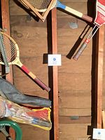 Assorted badminton and tennis rackets hanging on wall, part of racket covers and shuttlecocks visible