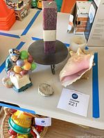 Group view of figurine, rectangular candle on stand, conch shell, geode