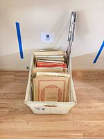 Overall view of bin filled with upright sheet music and folded metal stand