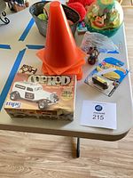 Overview showing model kit box, stack of cones, Hot Wheels car, bag of figures on table
