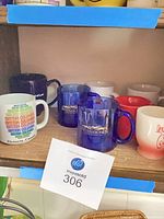 Shelf with multiple mugs including two blue Interlochen, white Victoria Canada mug, red mug, white mug with red script