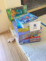 Stack of boxed puzzles with Giant Fire Truck, Mermaid and others plus tray puzzles behind