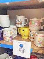 Shelf with eight assorted ceramic mugs including smiley face, floral, text, UCLA and embossed designs