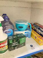 Shelf with Softsoap bottle, Spray Nine spray, Irish Spring soap box, Couvonda masks, By The Cup mug, wrap boxes