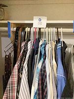 Row of assorted button-up shirts on hangers with belts at left