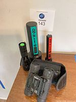 Group view of three flashlights and Bushnell binoculars with case