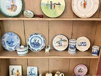 Front view of cabinet shelf with assorted plates, jars, figurine, mugs and tiles