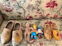 Both clog pairs and three plush/doll figures on floral couch