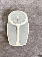 Top view of white/gray analog scale showing dial and footpads