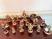 All 16 Hummel figurines grouped on tabletop, frontal view